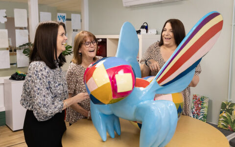 Three women gathered around a colourful bee sculpture