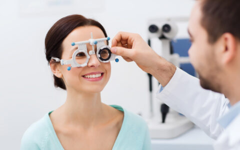 Head and shoulder shot of female looking happy, receiving an eye test with a pair of eye test spectacle tool.